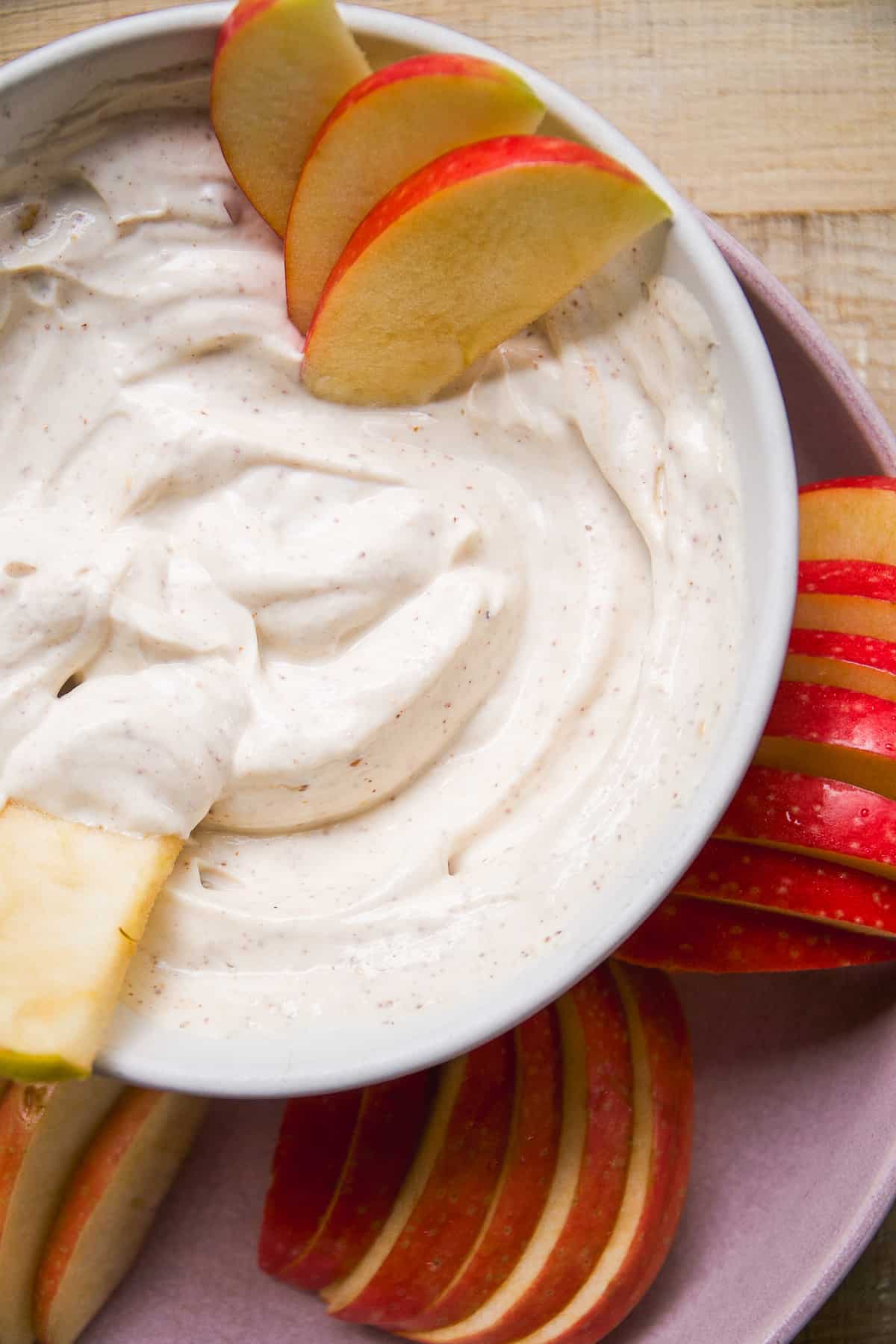 Bowl of yogurt fruit dip with apple slices on a purple plate.