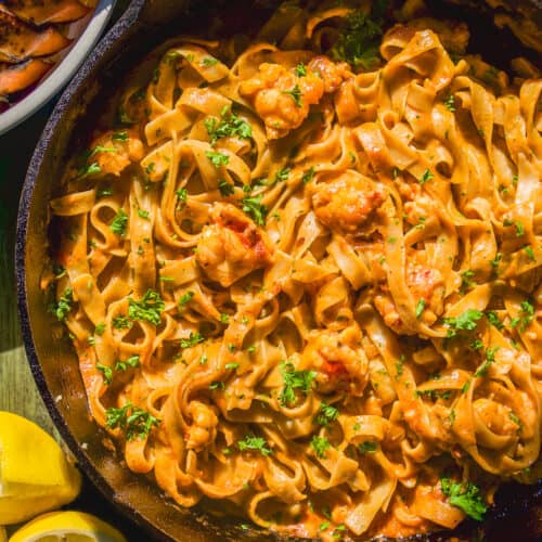 Lobster pasta in a skillet with herbs on a green surface.