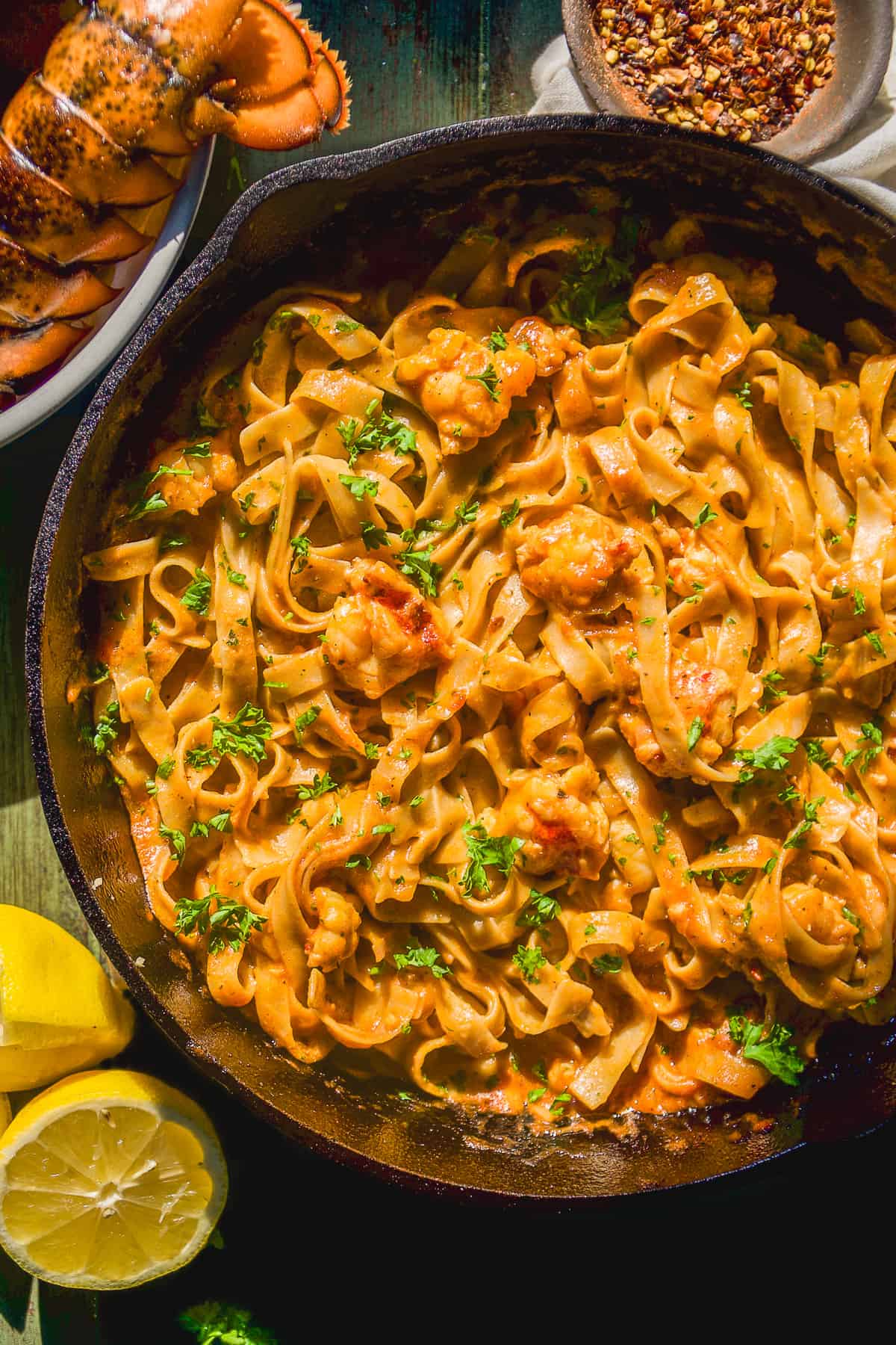 Lobster pasta in a skillet with herbs on a green surface.