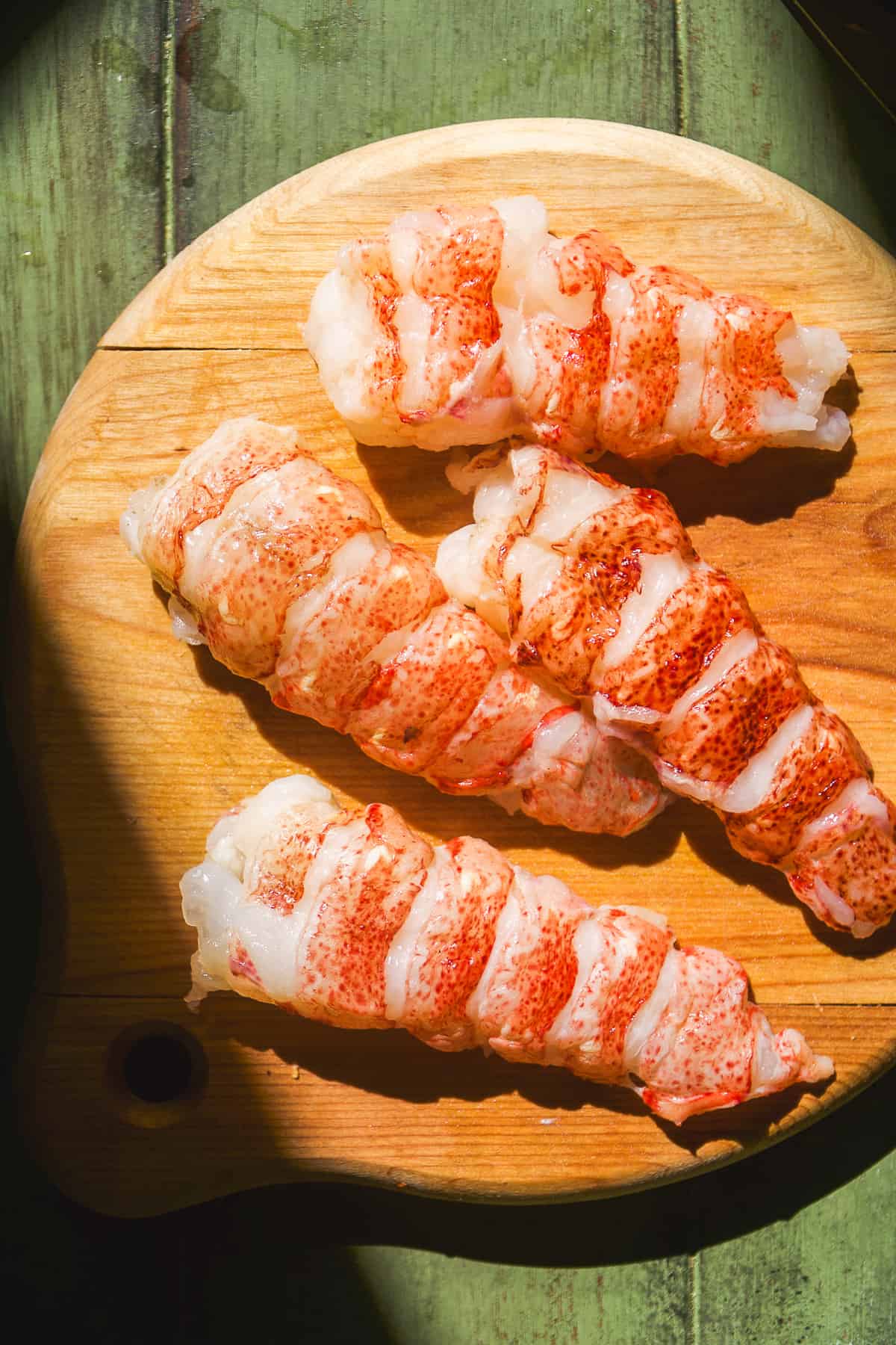 Lobster tail meat removed from the shell on a wooden board.