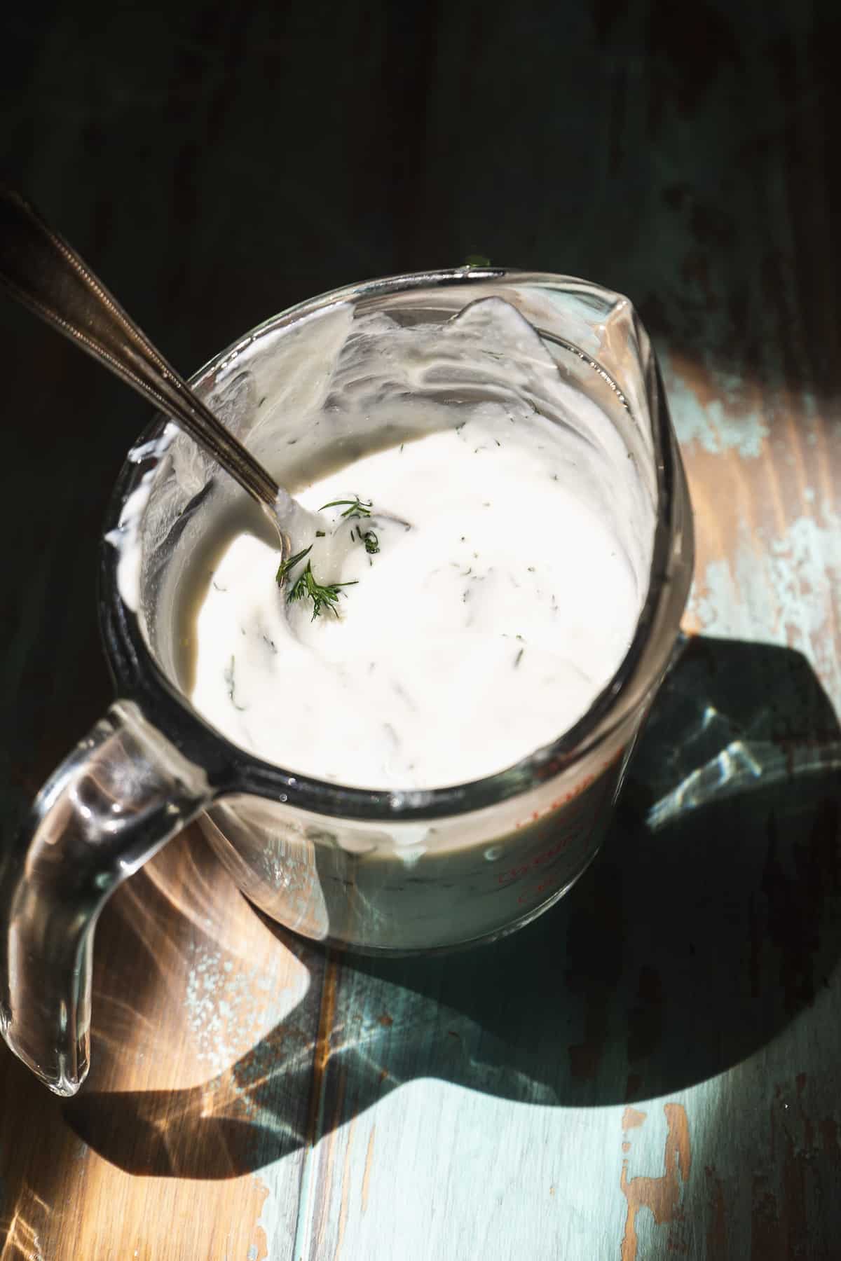 Greek yogurt mixed with dill and herbs in a glass cup.