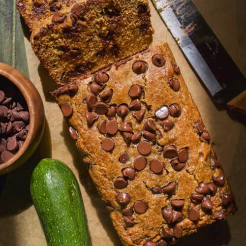 Zucchini chocolate chip bread on parchment paper with a few slices cut out.