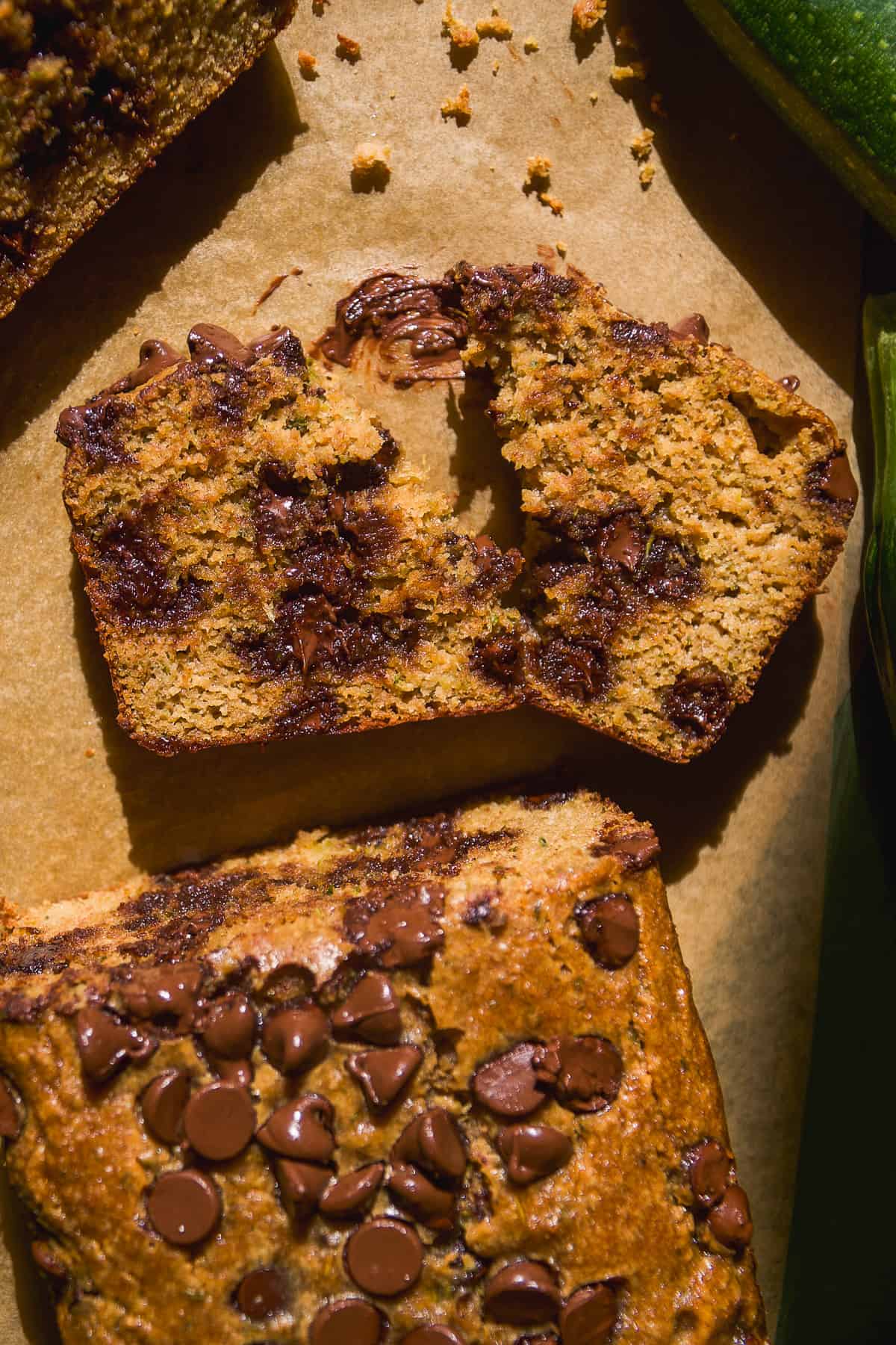 Chocolate chip zucchini bread slice broken in half on parchment paper.