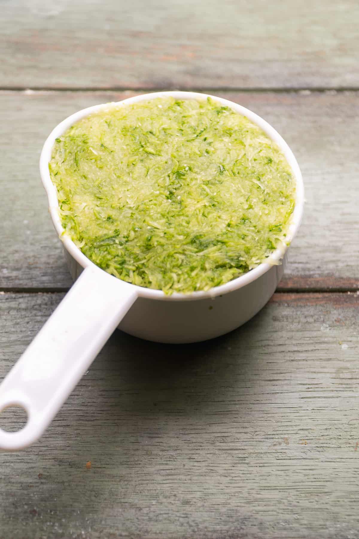 Grated zucchini in a measuring cup.