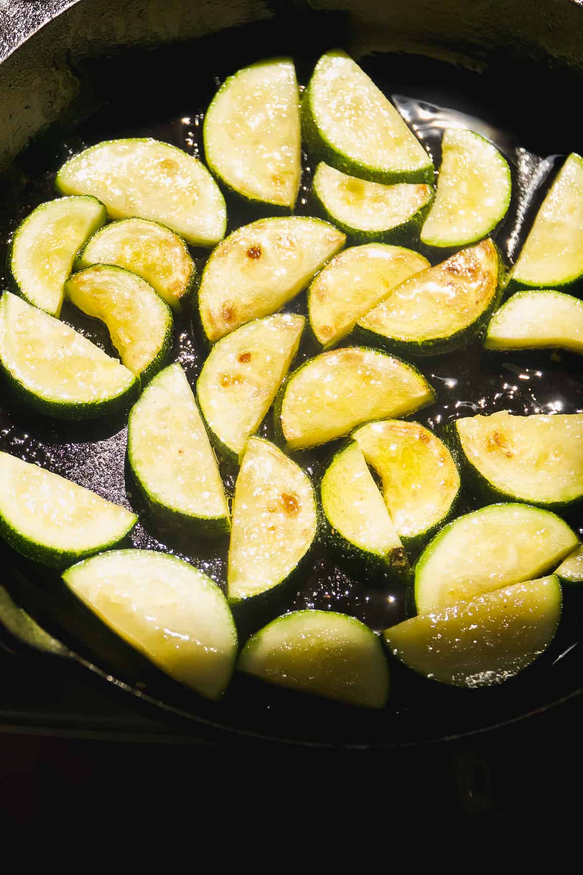 Zucchinis roasting on a cast iron skillet.