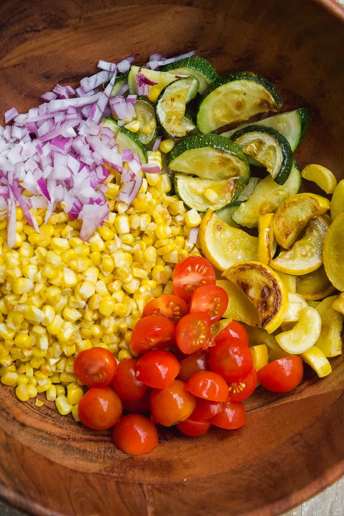 Grilled vegetables in a wooden bowl about to be tossed together.