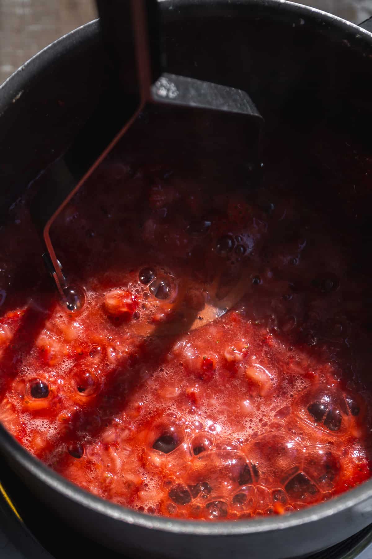 Strawberries cooking in a pot with a masher.