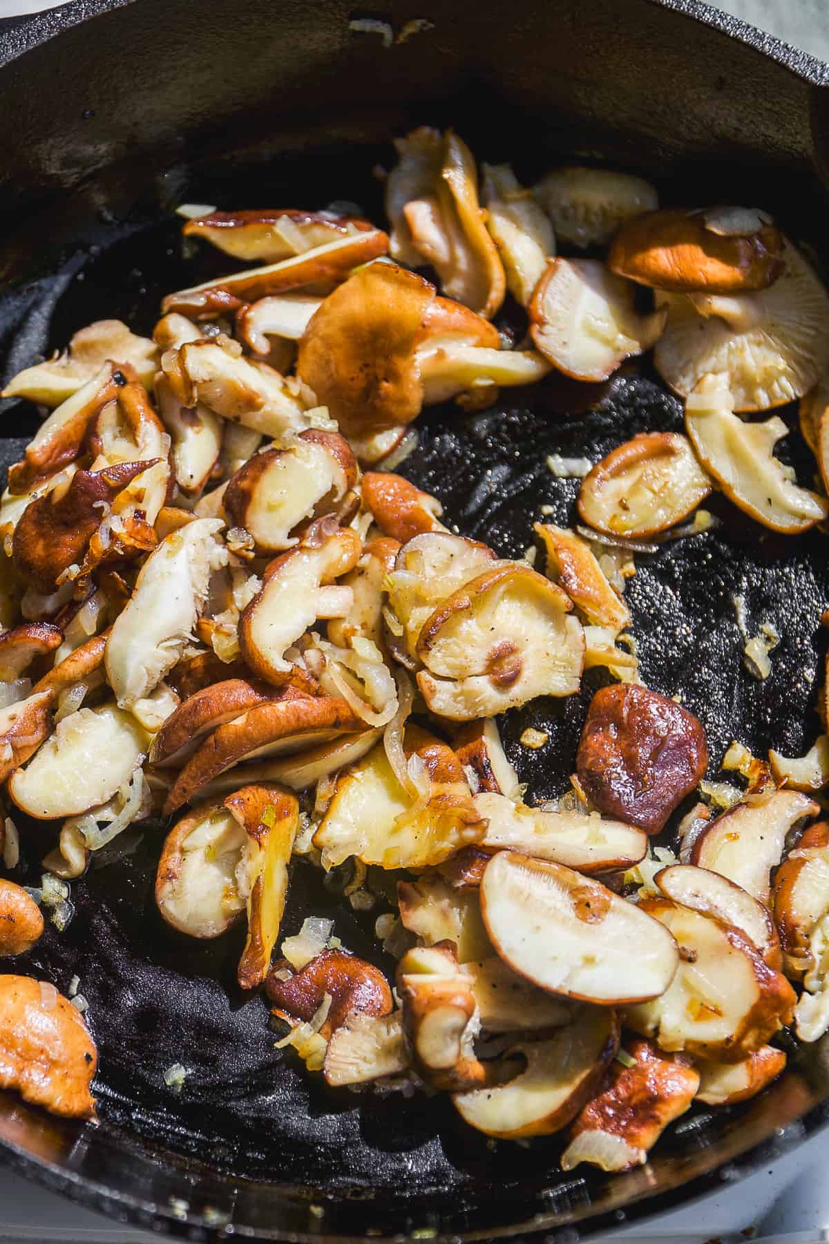 Mushrooms cooking in a cast iron skillet.