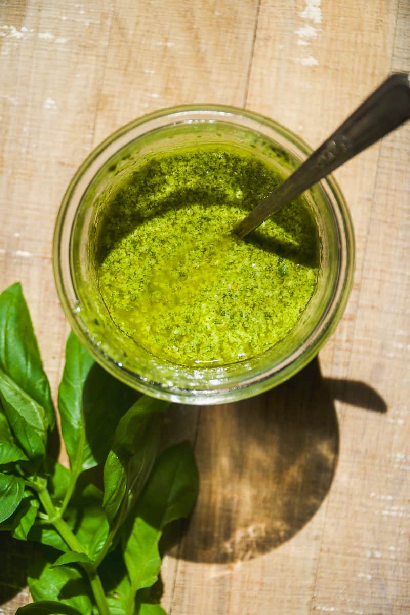 Dairy free basil pesto in a jar on a wooden surface.