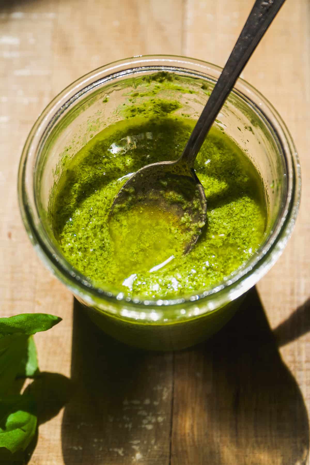 Dairy free pesto in a glass jar with a spoon.