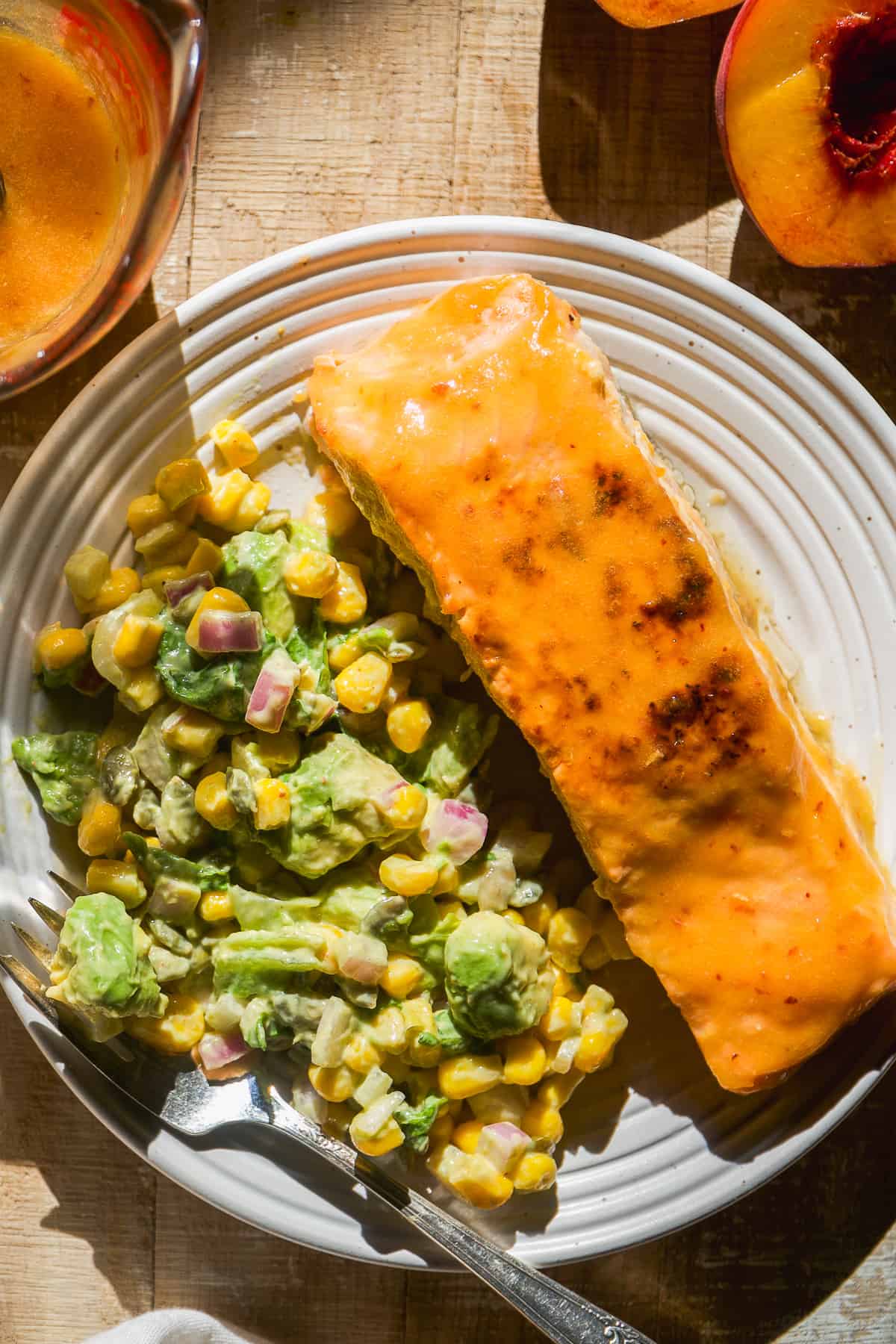 Peach glazed salmon on a plate with an avocado green salad.