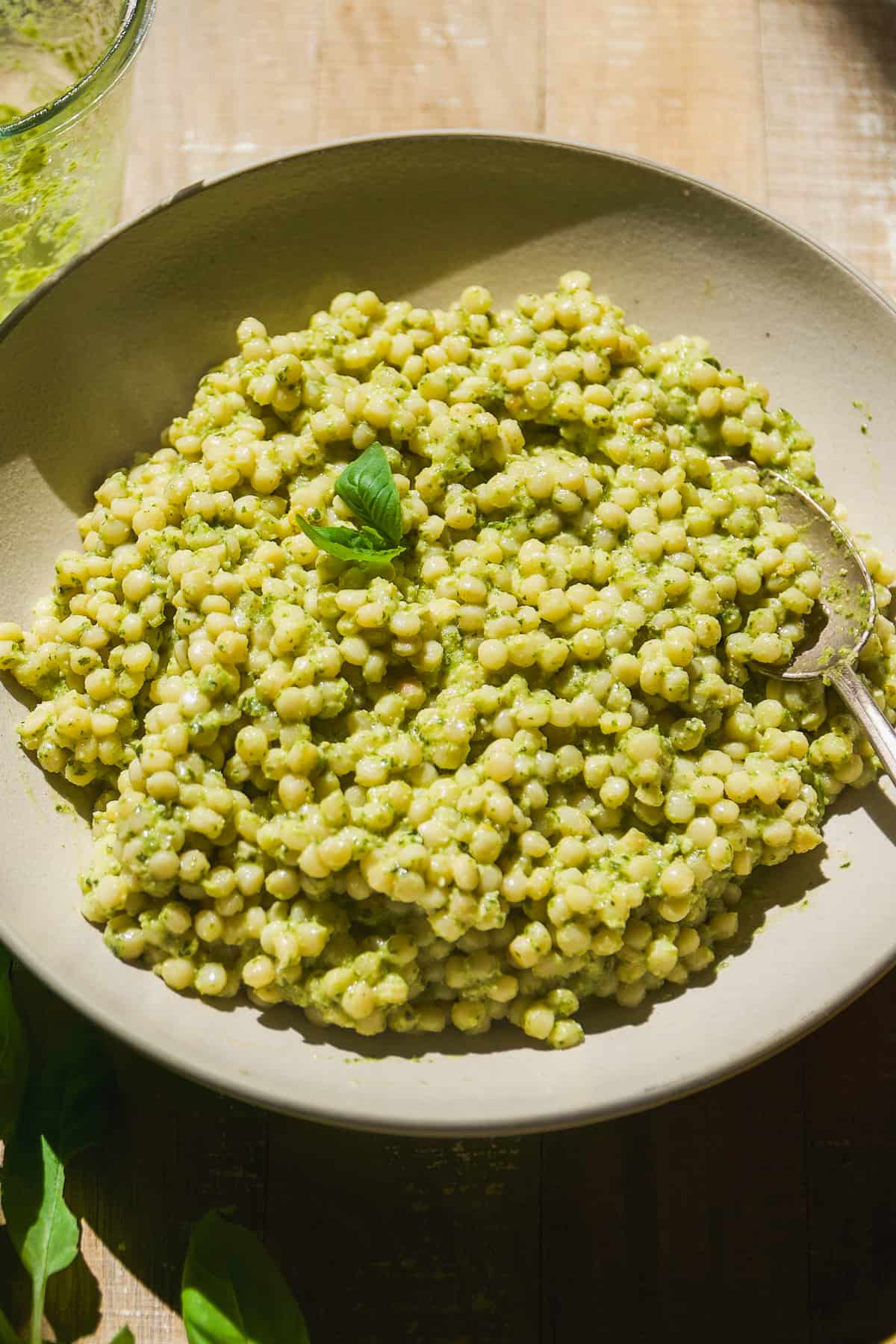 Dairy free pesto couscous in a tan bowl with a spoon.