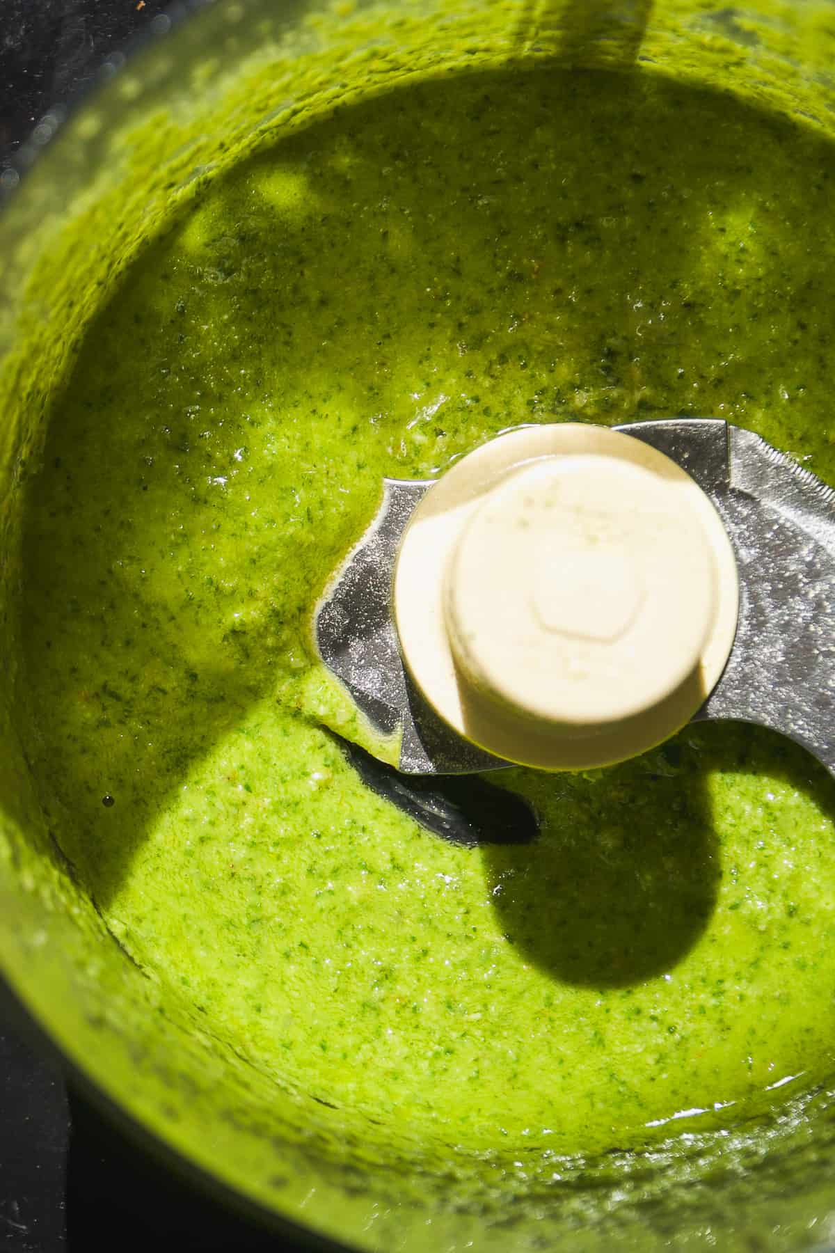 Up close view of basil dairy free pesto in a food processor.
