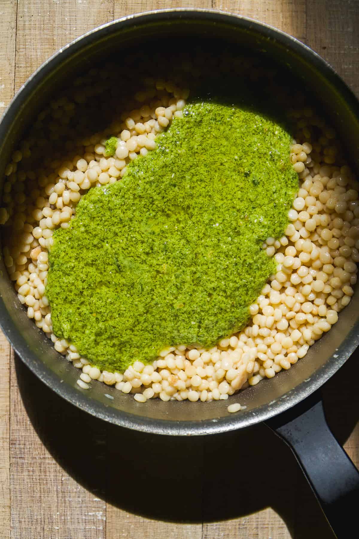 Couscous about to be tossed with pesto sauce in a pot.