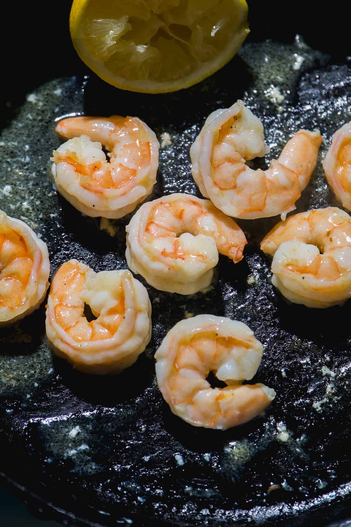 Shrimp cooking on a cast iron skillet with lemon.