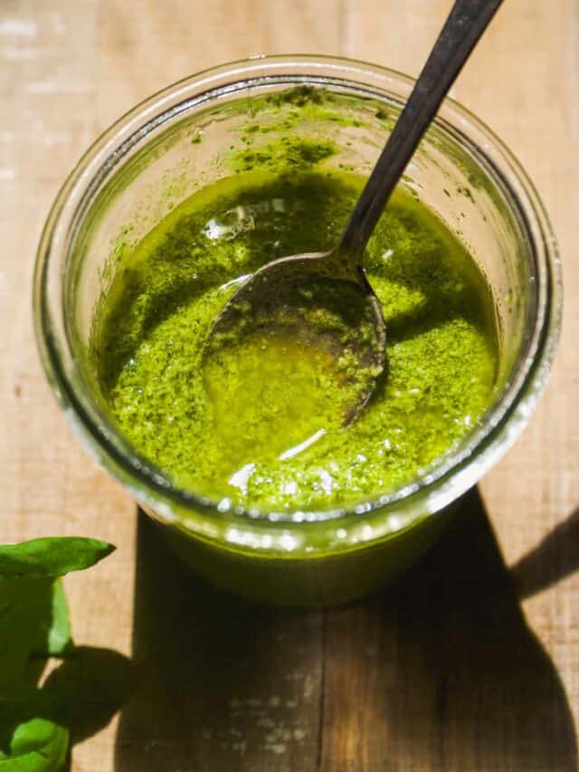 Dairy free pesto in a glass jar with a spoon.