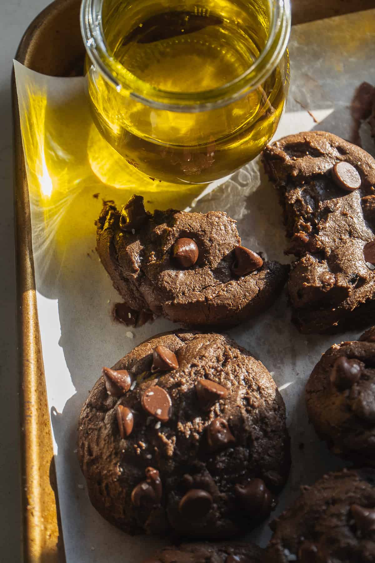 Olive oil cookies with chocolate chips on a baking sheet with a jar of olive oil.