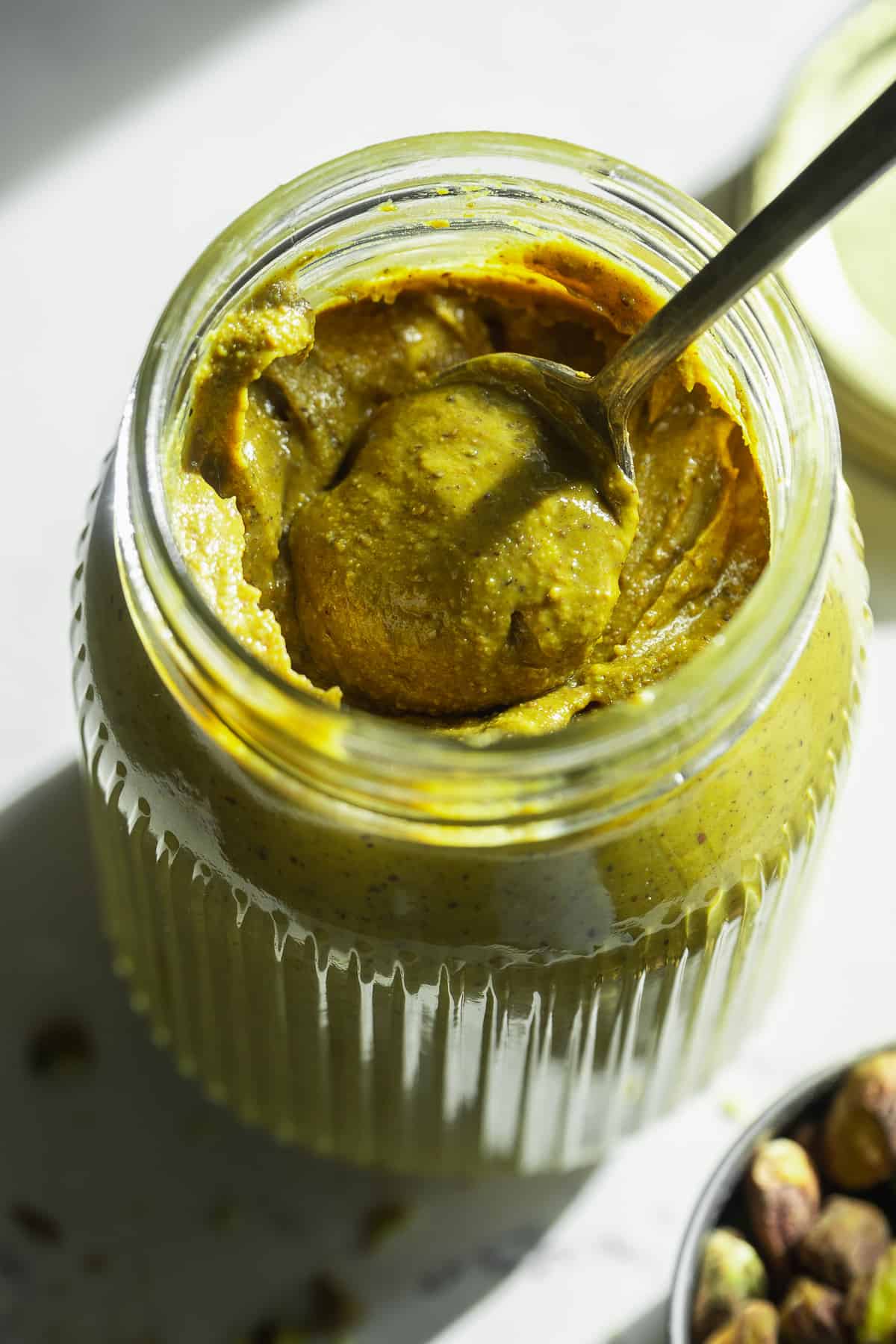 Pistachio butter in a glass jar with a spoon inside.