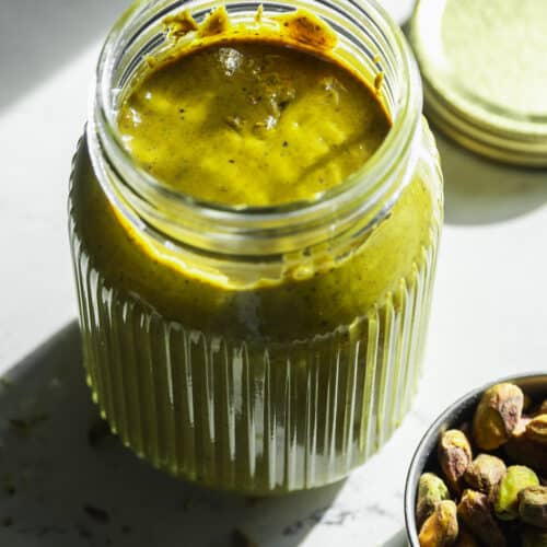 Glass jar of pistachio butter with the lid off.