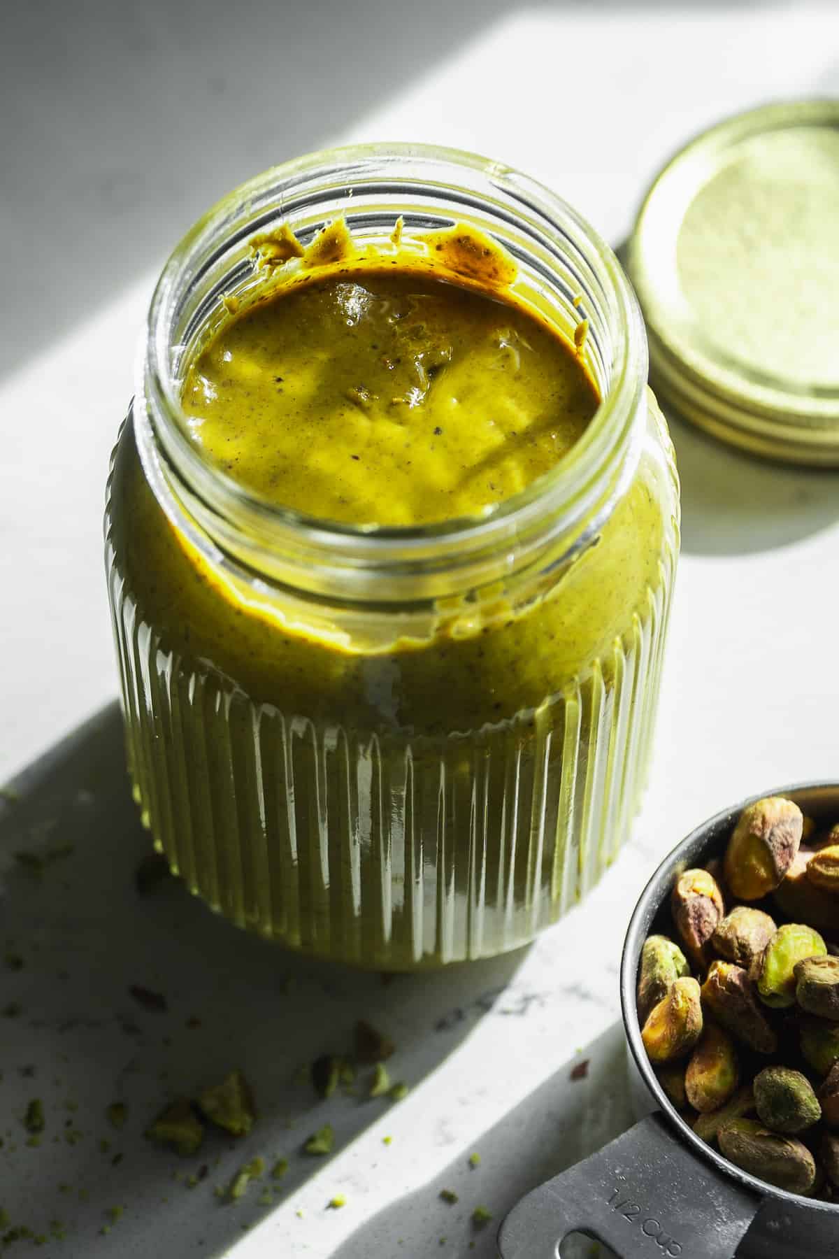 Glass jar of pistachio butter with the lid off.