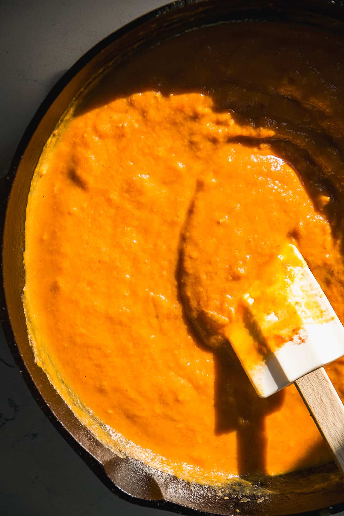 Pumpkin marinara sauce cooked in a skillet with a rubber spatula.