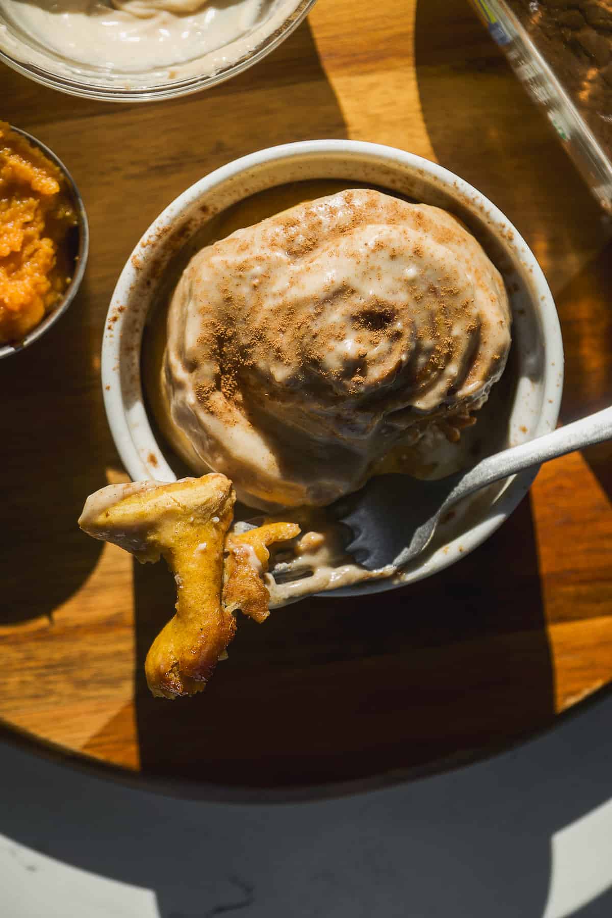 Pumpkin spice cinnamon roll in a single dish with a fork taking a bite.
