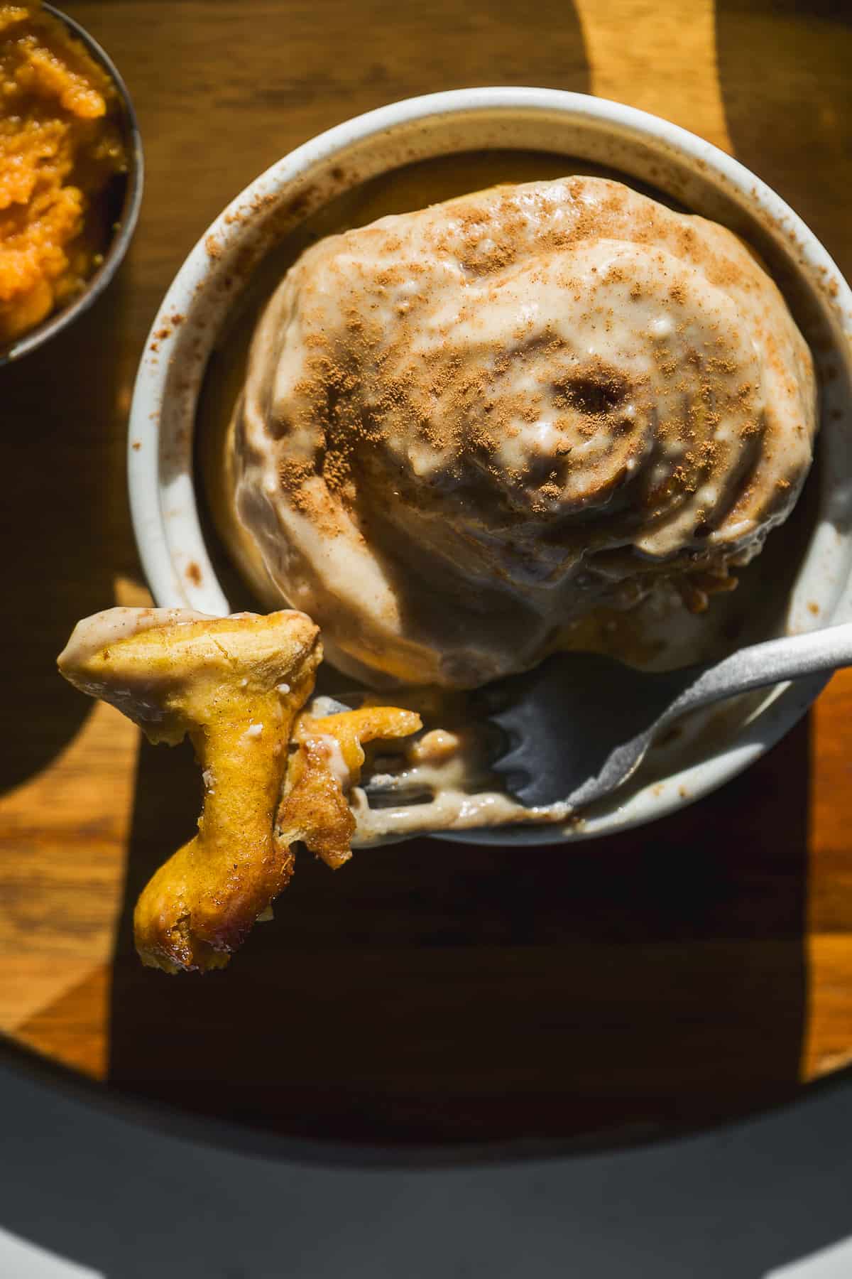 A fork taking a bite out of a single serve cinnamon roll.