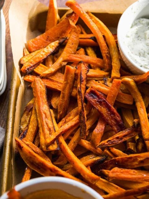 Aerial view of baked sweet potato fries on a baking sheet with dipping sauce
