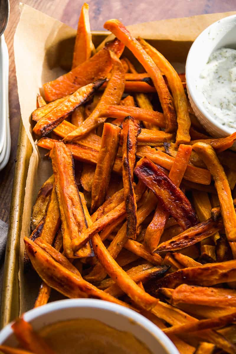 Aerial view of baked sweet potato fries on a baking sheet with dipping sauce