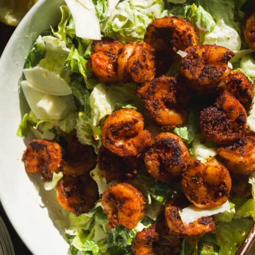 Caesar salad with blackened shrimp on top in a large bowl.