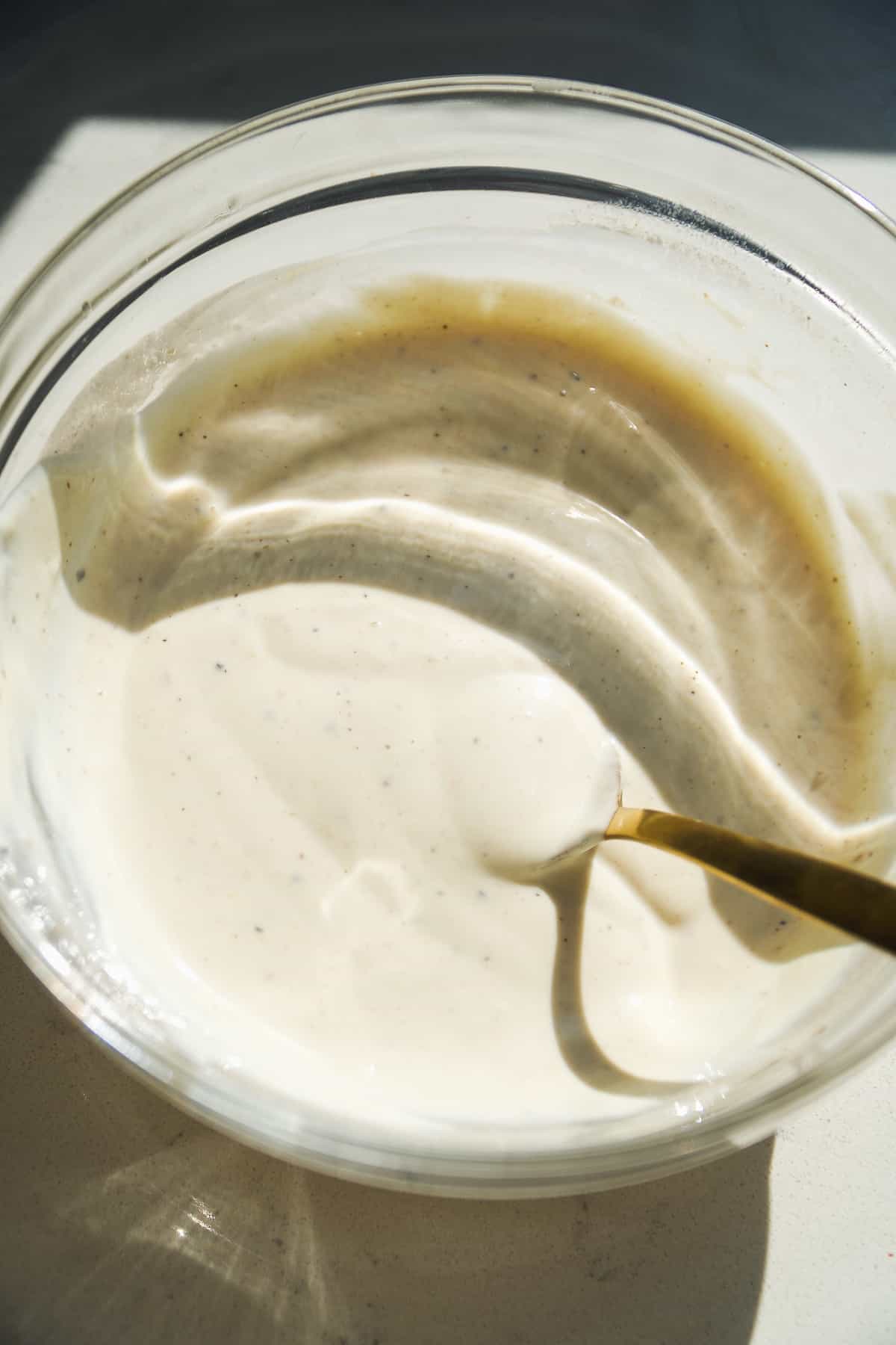 Greek yogurt caesar dressing mixed in a clear bowl with a spoon.