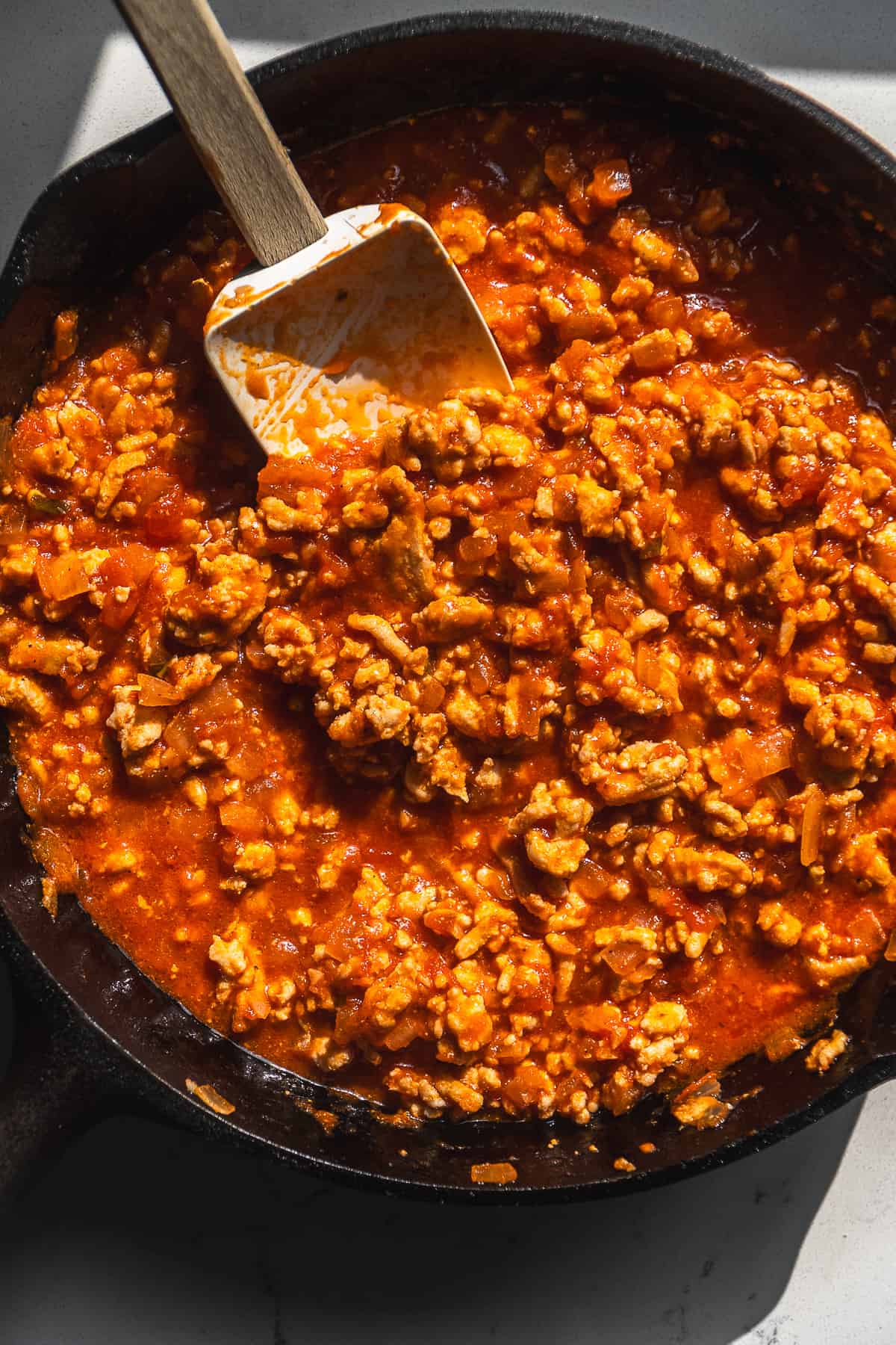 Marinara mixed into ground turkey in a cast iron skillet.