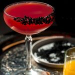 Pomegranate margarita in a tall glass with black sea salt on a platter.