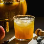 Spiked apple cider punch in a glass with the bowl behind.