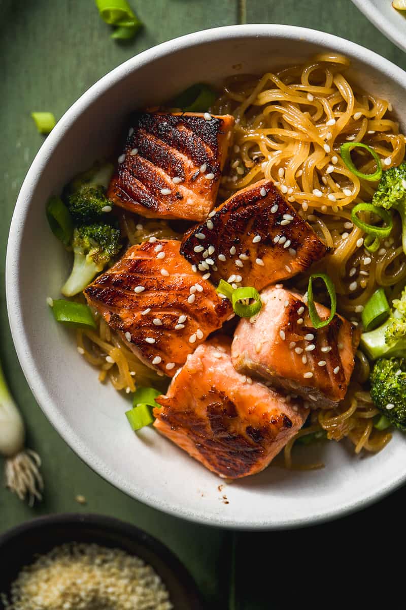 Teriyaki salmon noodles in a white bowl on a green surface