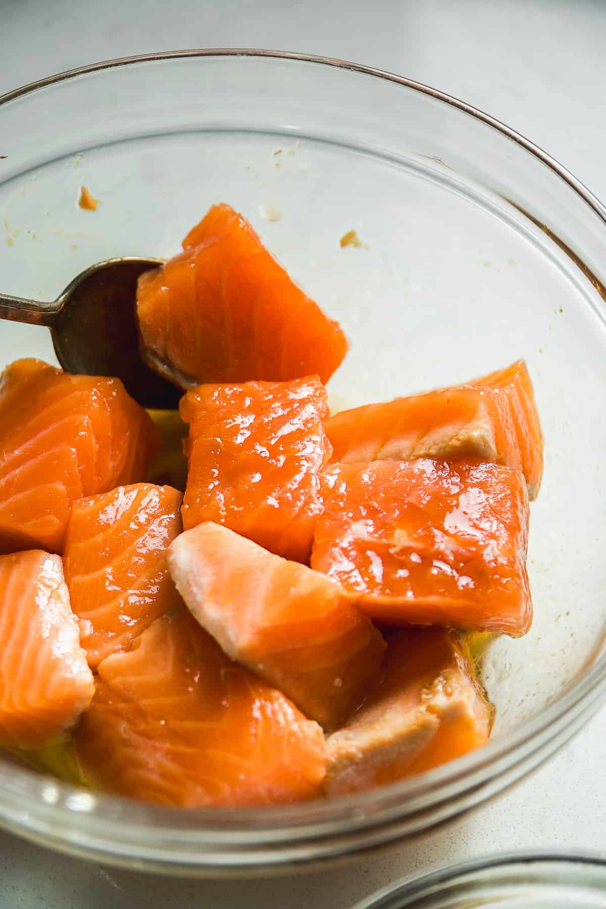 Salmon bites tossed in teriyaki sauce in a glass bowl.