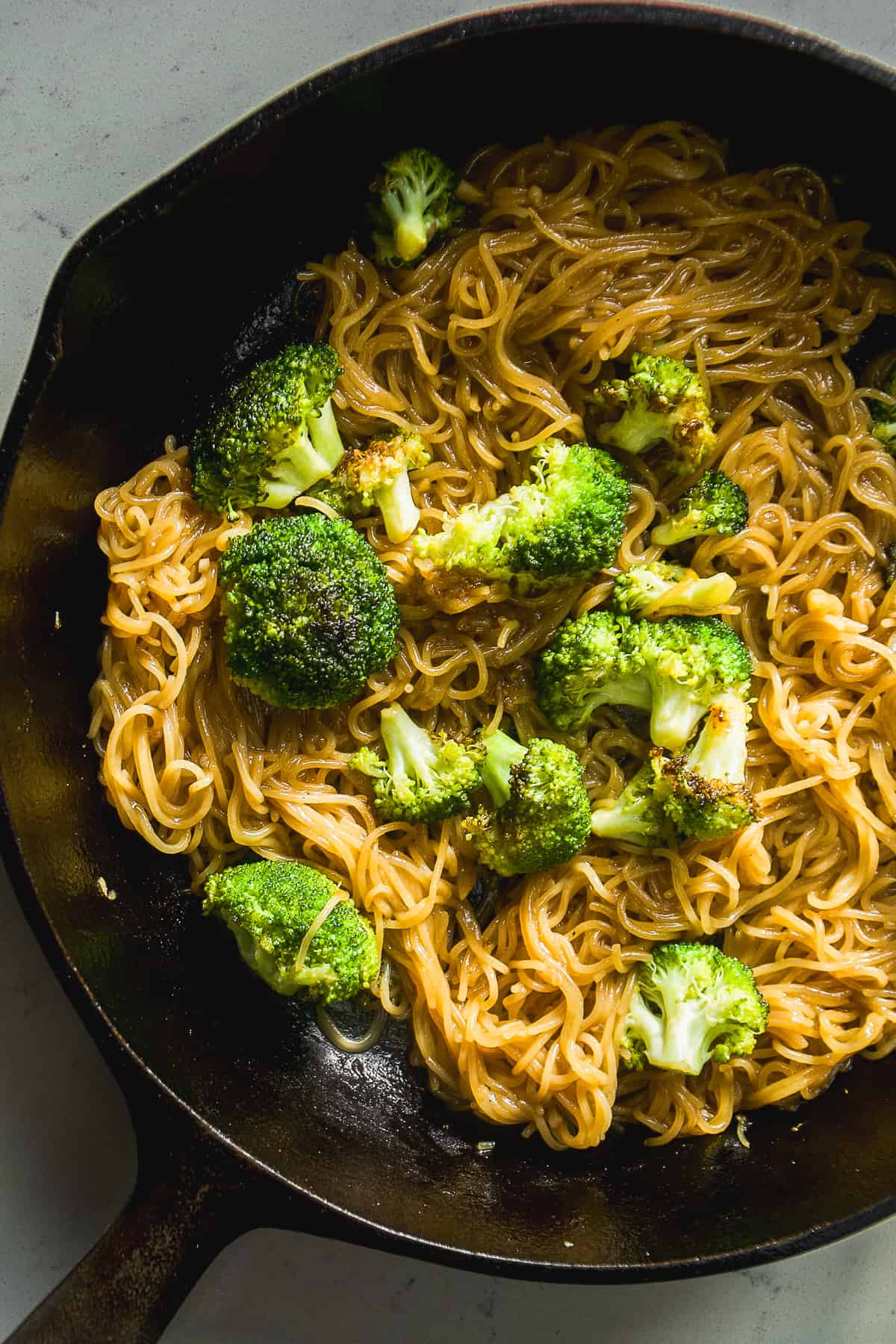 Broccoli on top of teriyaki noodles in a skillet.