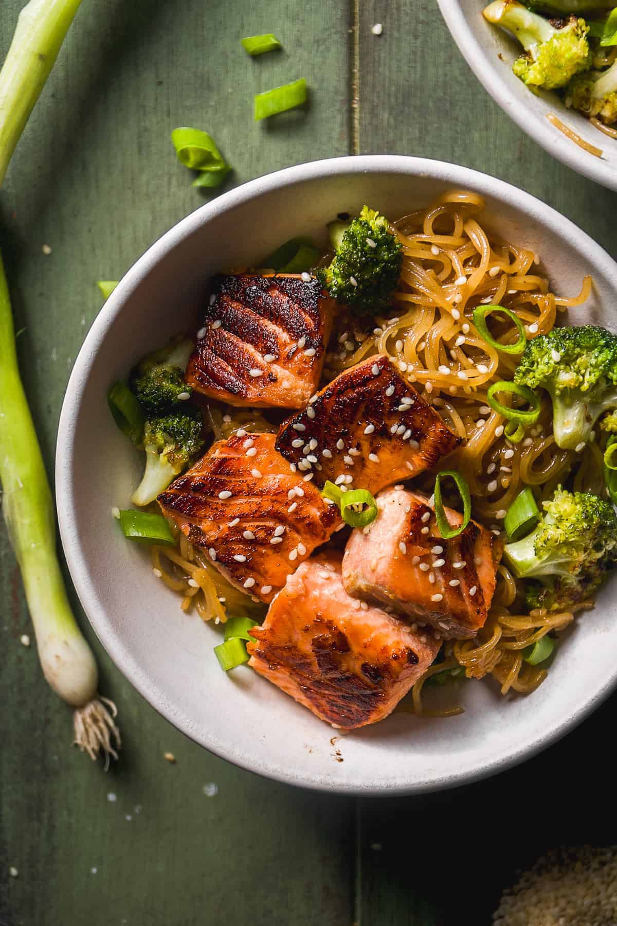 Overhead view of a bowl of teriyaki noodles with salmon bites on top.