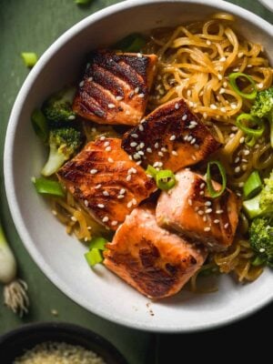 Bowl on teriyaki salmon noodles with broccoli with sesame seeds on top.