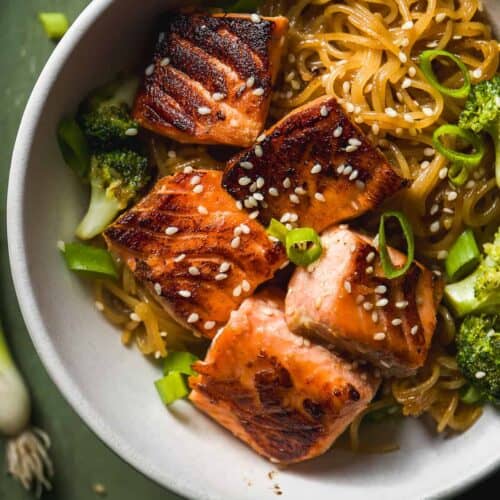 Bowl on teriyaki salmon noodles with broccoli with sesame seeds on top.