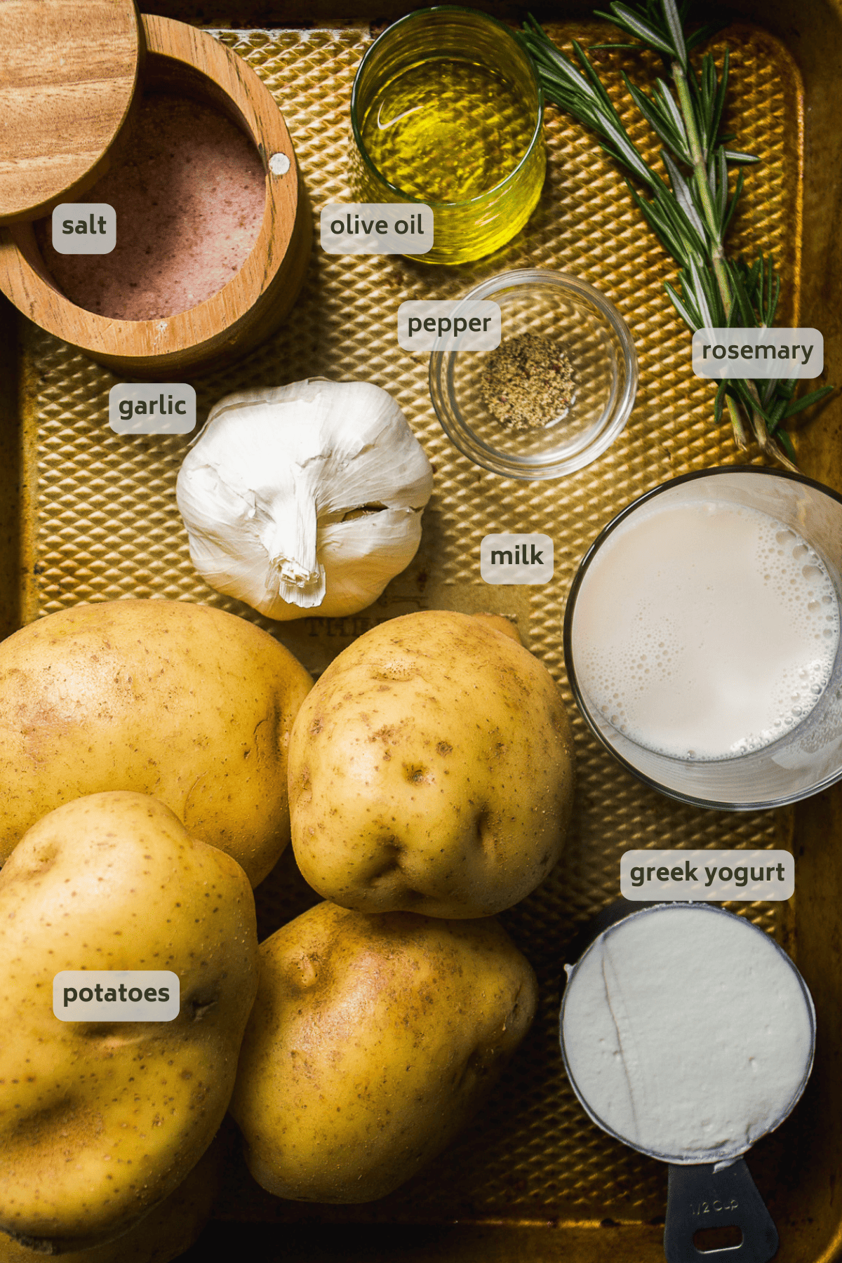Garlic mashed potatoes ingredients on a gold baking sheet with ingredients labeled.