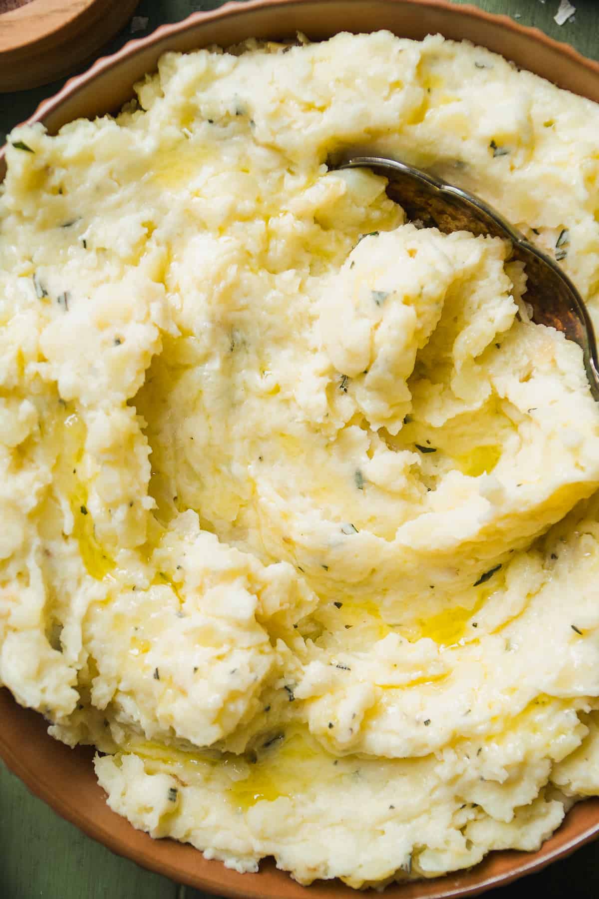 Up close view of garlic mashed potatoes in a large brown serving bowl.