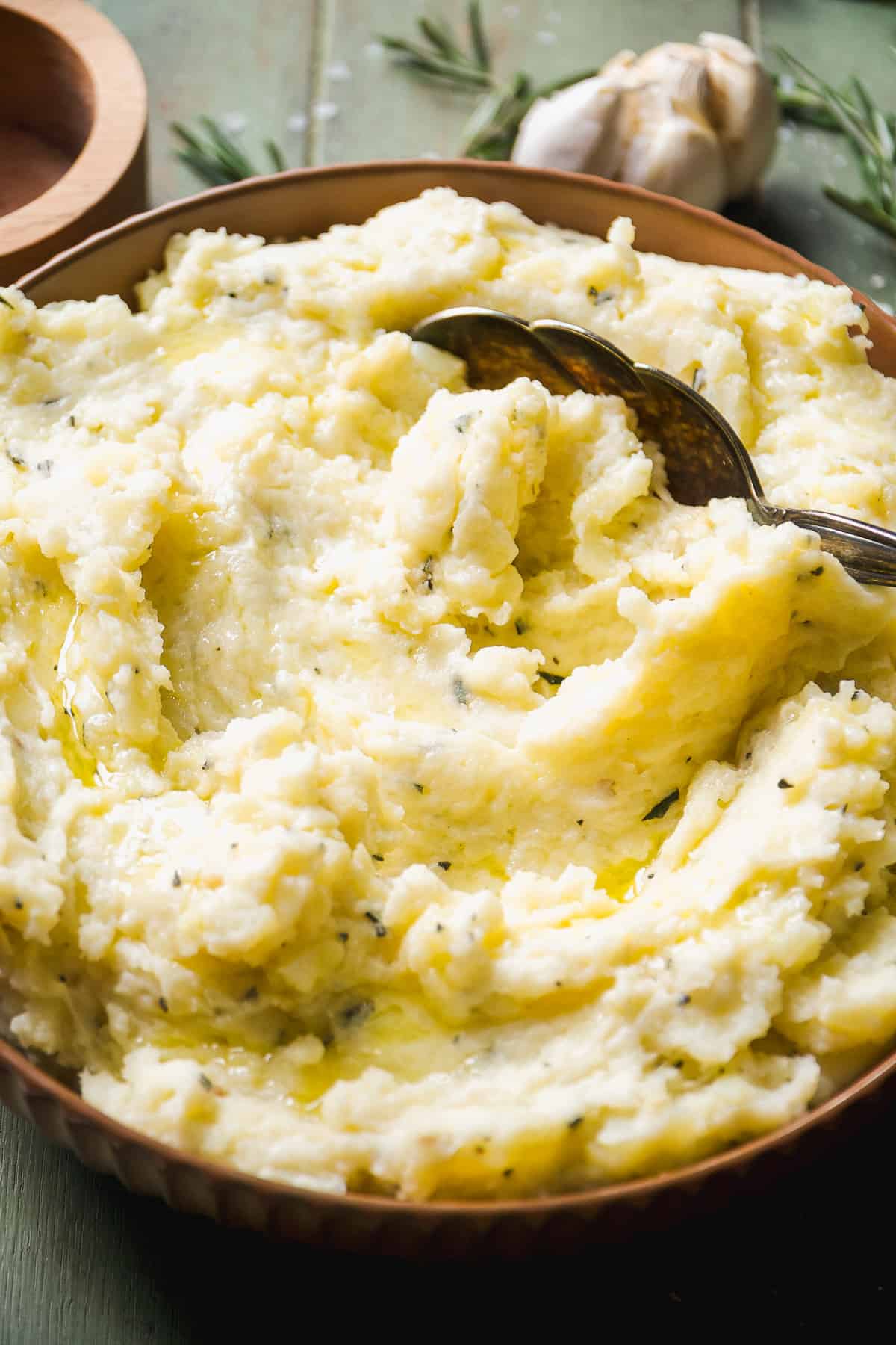 Brown bowl with garlic mashed potatoes inside and a large spoon resting inside.