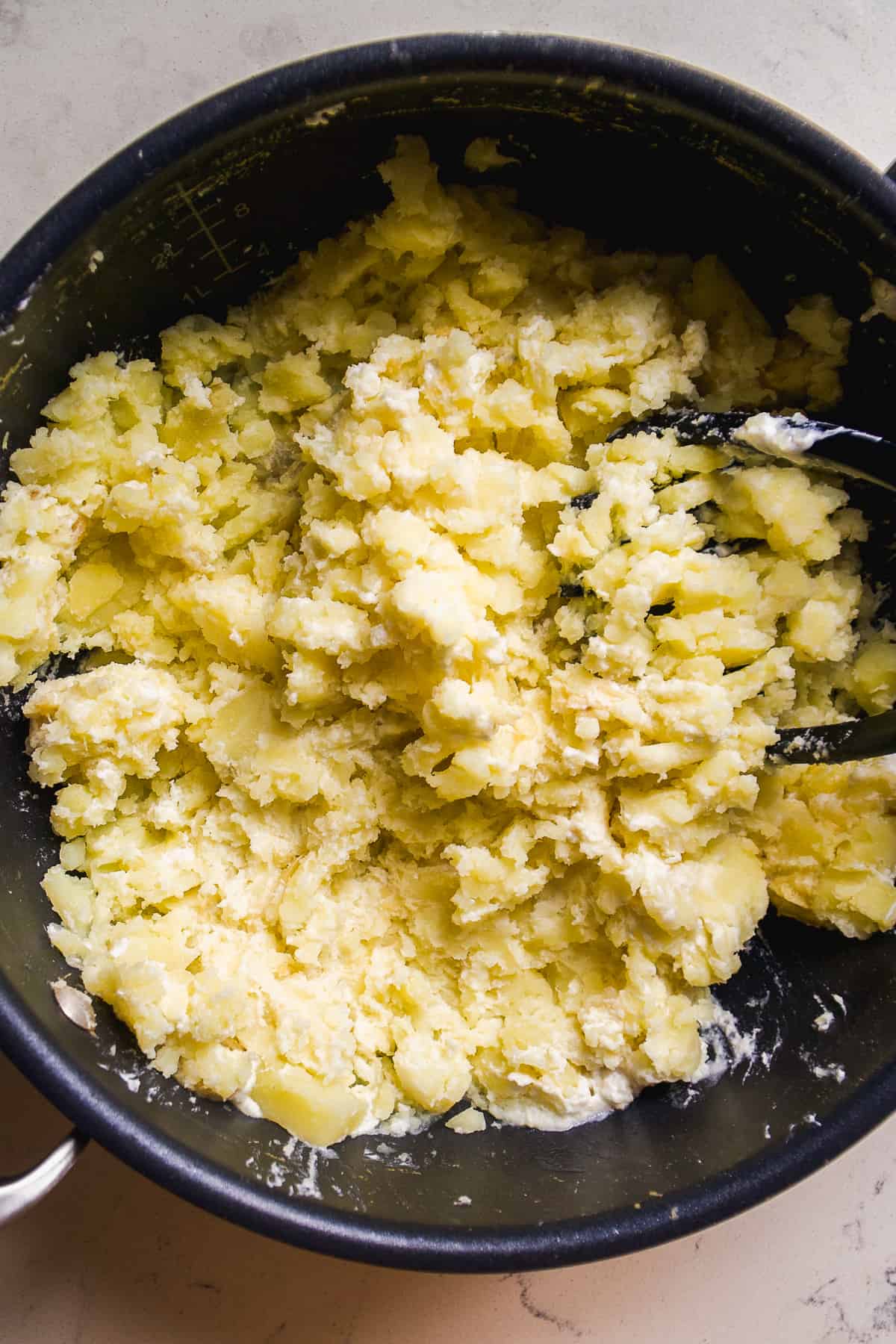 Potatoes mashed in a pot with a potato masher.