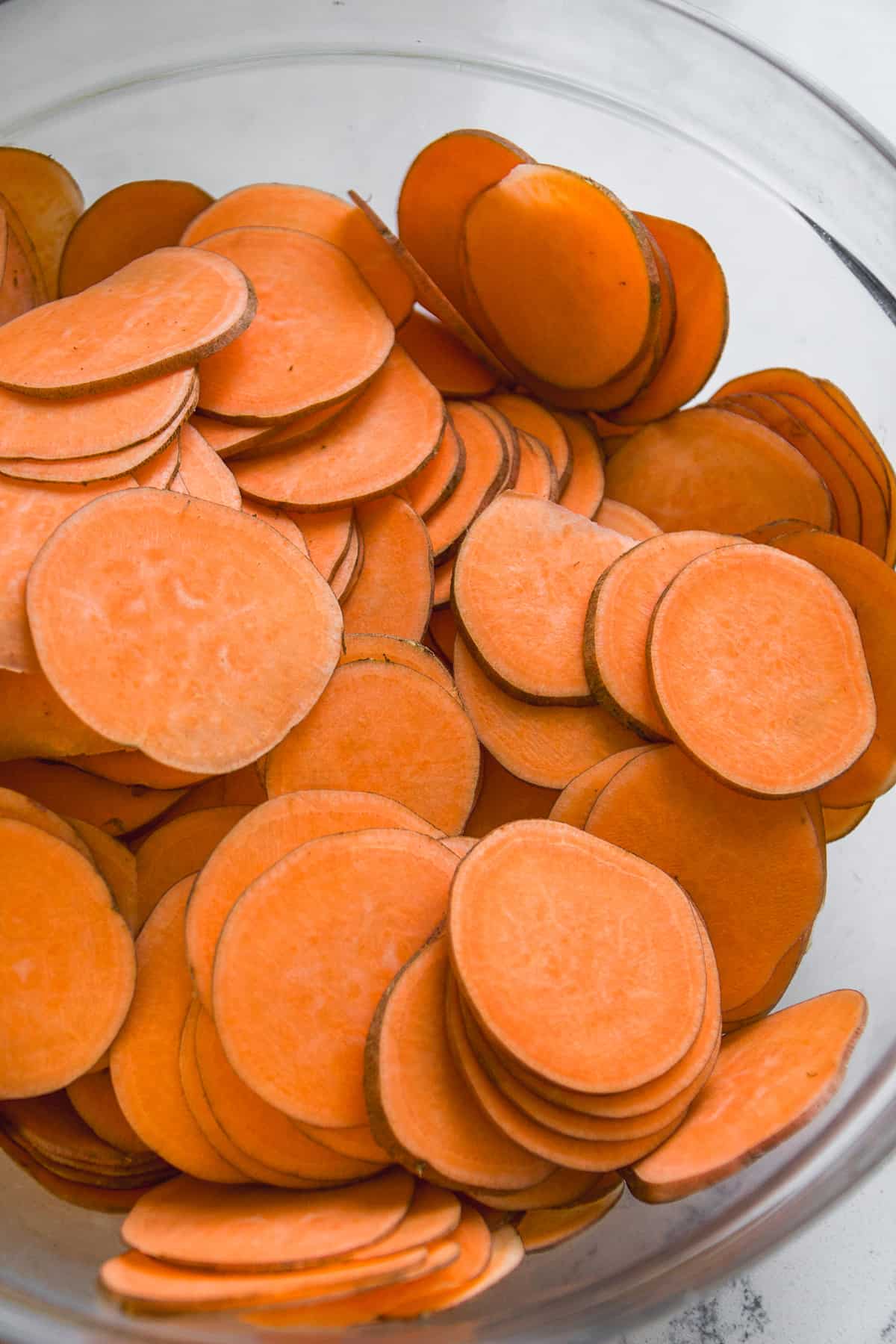 Thin scalloped sweet potatoes in a glass bowl.