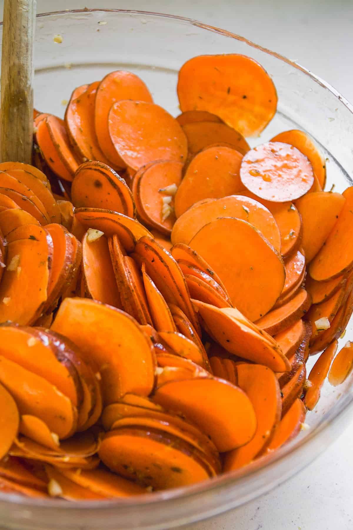 Thin sweet potato rounds in a glass bowl tossed in olive oil and spices.