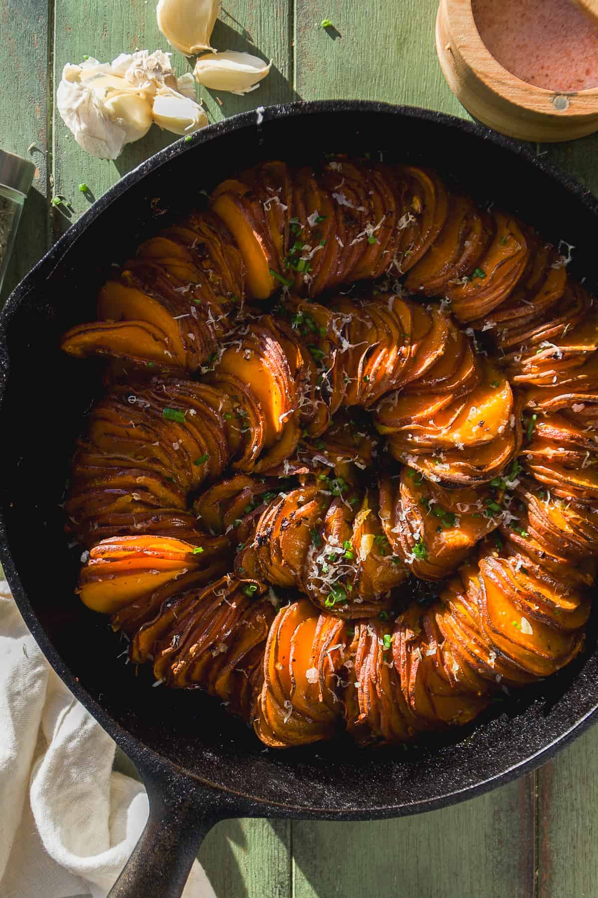 Cast iron skillet with scalloped sweet potatoes in a spiral.