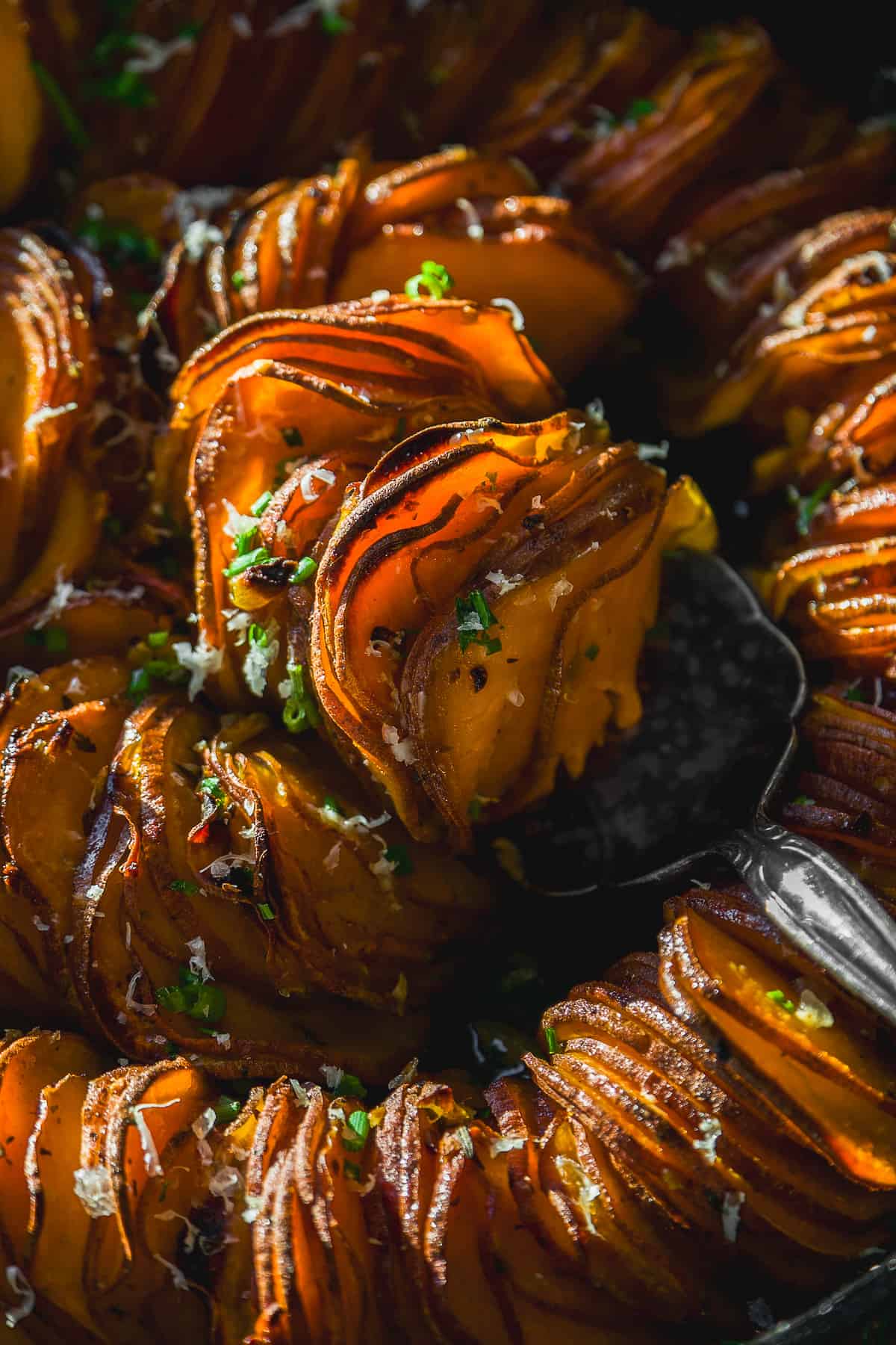 Scalloped sweet potatoes in a skillet with a serving spoon.