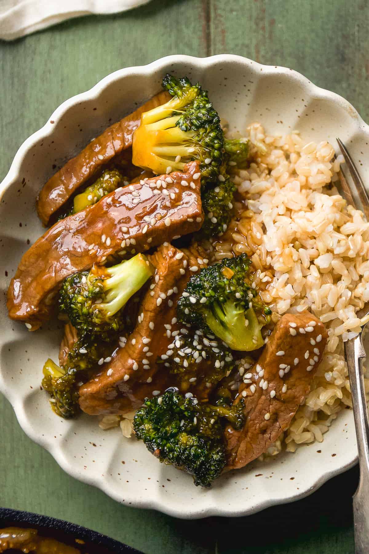 Overhead view of a bowl of beef and broccoli with sesame seeds and rice.