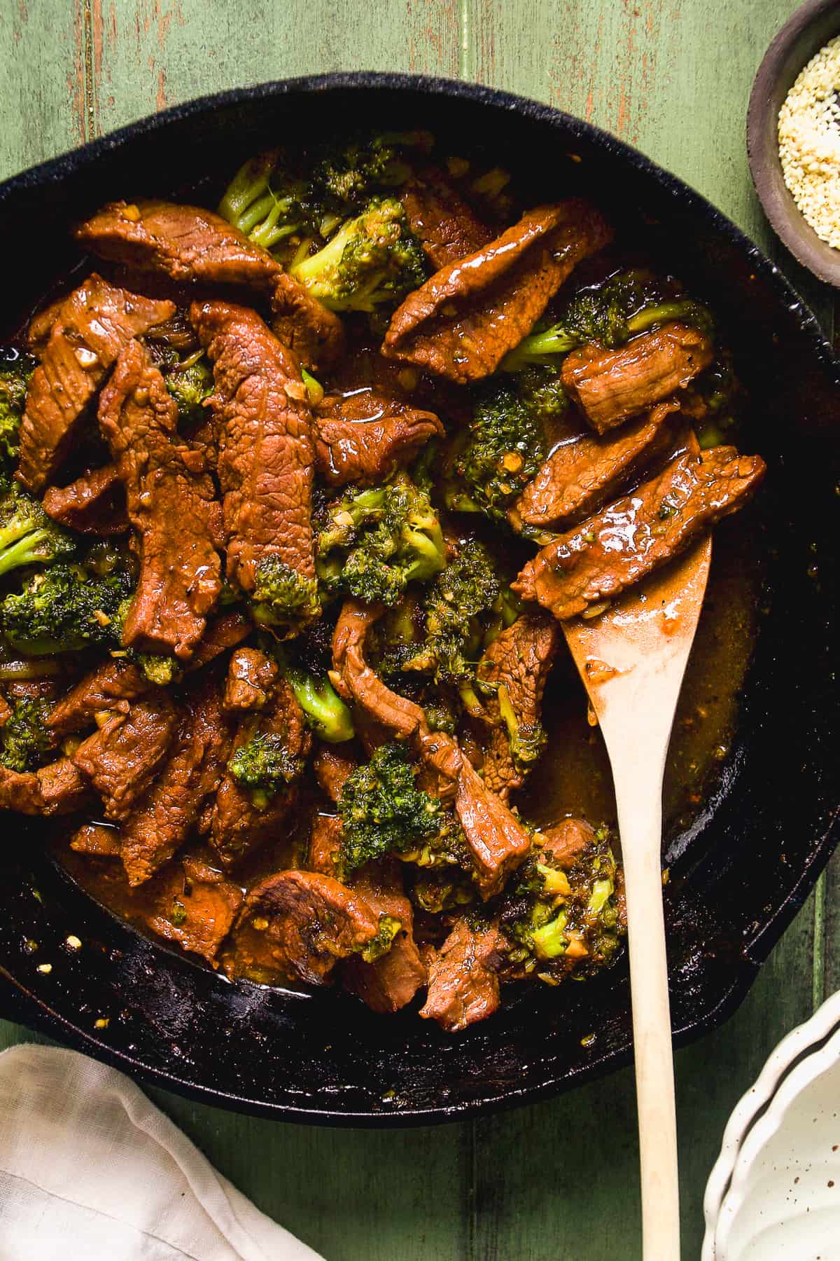 Overhead view of beef and broccoli in a cast iron skillet with a wooden spoon.